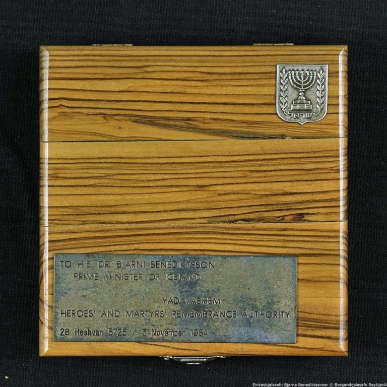 Tréaskja með peningi. Á öskjunni stendur: TO H.E. DR. BJARNA BENEDIKTSSON PRIME MINESTER OF ICELAND. YAD VASHEM. HEROES AND MARTYRS REMBRANCE AUTHORITY 28 Hesthavn 5725, 3. November 1964. Líklega frá opinberri heimsókn Bjarna Benediktssonar til Ísraels í nóvember 1964.