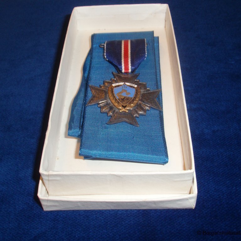 Askja með silkiborða og stjörnu. Á stjörnunni stendur ISI 1912 til 1962. Íþróttasamband Íslands sæmdi dómsmálaráðherra Bjarna Benediktsson 50 ára afmælisheiðursmerki sambandsins 29. janúar 1962.