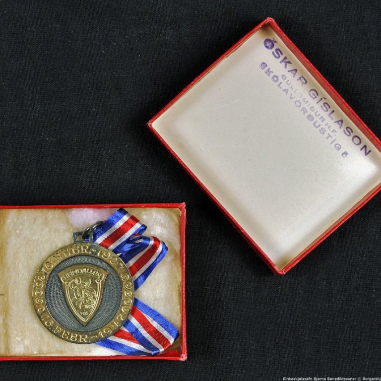 Askja með peningi og silkiborða.

Á framhlið peningsins stendur: HEIMDALLUR. FÚF. 16. FEBRÚAR 1927, 16. FEBRÚAR 1947.

Á bakhlið peningsins stendur: BJARNI BENEDIKTSSON UTANRÍKISRÁÐHERRA.