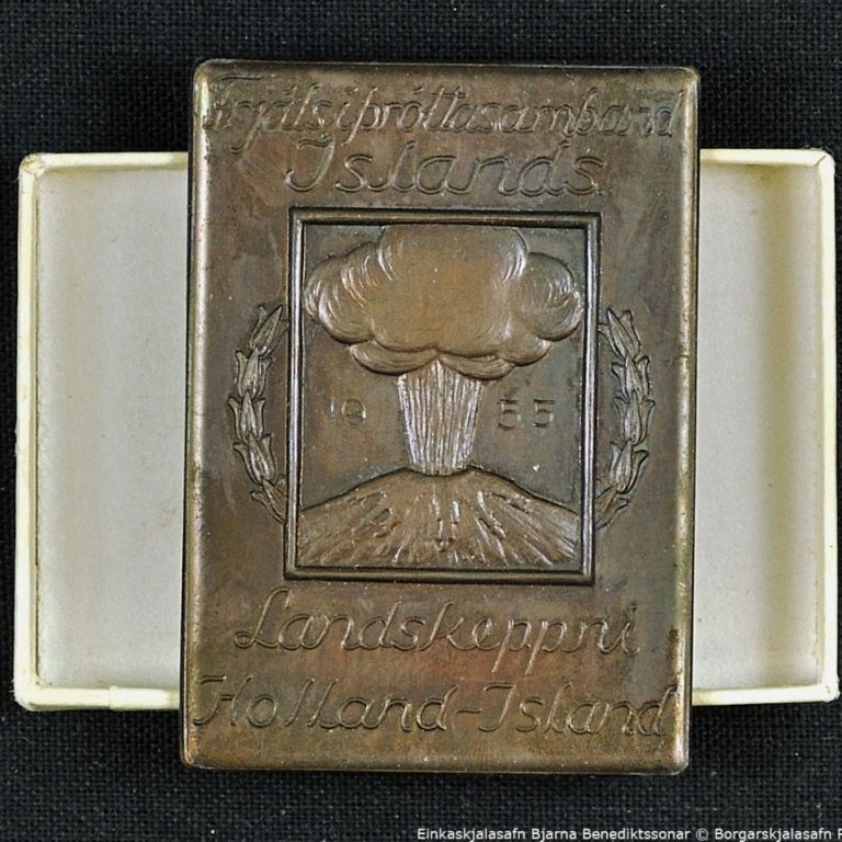 Askja með merki.

 

Á merkinu stendur: Frjálsíþróttasamband Íslands. 1955. Landskeppni Holland-Ísland.