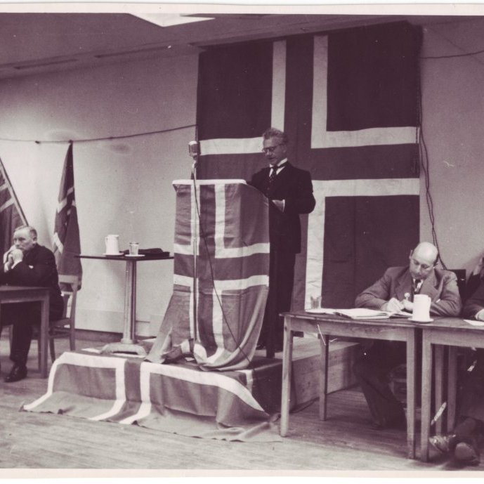 Ólafur Thors í ræðustól á Landsfundi Sjálfstæðisflokksins í Valhöll á Þingvöllum 1943. Til vinstri situr Pétur Magnússon fundarstjóri, en til hægri þeir Gunnar Espólín og Friðrik Þórðarson.